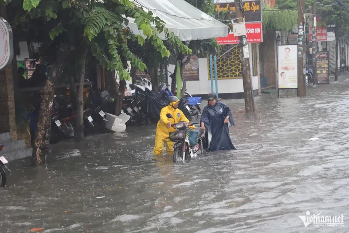 Một số xe chết máy khi chạy qua đoạn đường nước ngập nửa mét. Trong ảnh là bà Hồ Thị Bé (62 tuổi) được nhân viên công ty thoát nước đô thị TPHCM hỗ trợ đẩy phương tiện thoát khỏi 